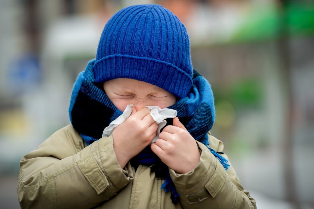 little boy sneezing into tissue