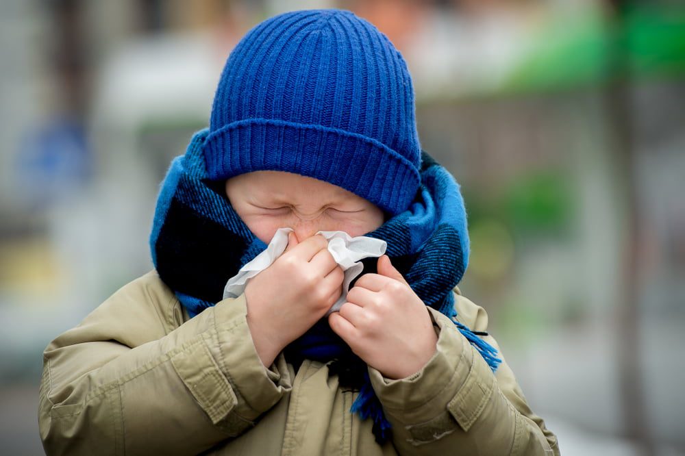 little boy sneezing into tissue